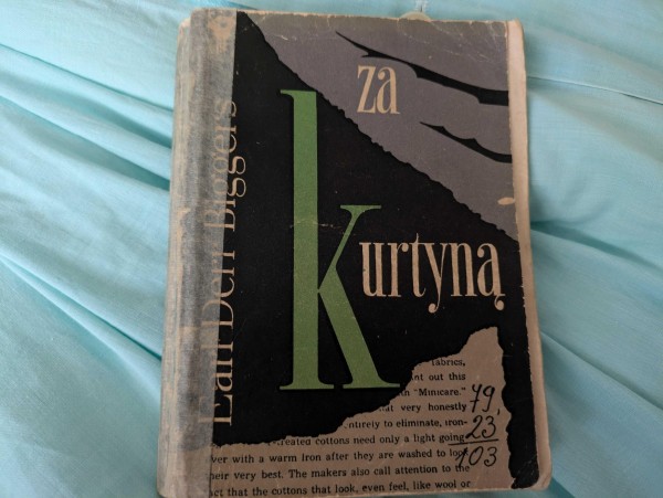 Zdjęcie okładki książki "Za kurtyną" Earla Derra Biggersa. Książka jest zniszczona, ale widać tytuł, kawałek angielskiego tekstu na dole, nazwisko autora, a także niepoprawne działanie pisemne 79 + 23 = 103.