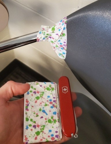 Photo of a plastic and metal chair with its back taped onto the arm that used to support it, with a hand holding the card roll of tape and a victorinox swiss army knife