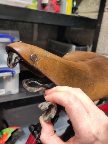 A very old and saggy Brooks saddle, on a bicycle, next to some shelves (safely back home, in other words)

The leather nose is lifted off the frame, and I'm holding up a loose part that was still clinging on. The nose bolt has sheared or stripped its threads, and has fallen off, causing the entire structure to become unworkable and no longer possible to ride comfortably. Even saggier than normal.

RIP good, comfy saddle that might be as old as I am.