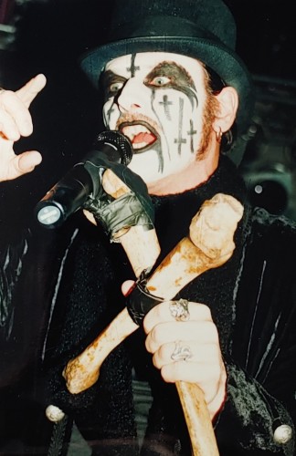 Wokalist King Diamond w "trupim" makijażu scenicznym, trzymający w ręku statyw mikrofonu zrobiony z dwóch sklejonych na krzyż kości.