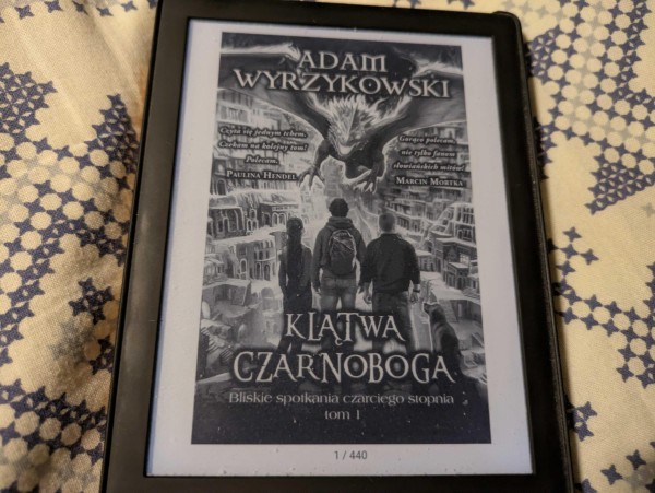 Okładka e-booka "Klątwa Czarnoboga" Adama Wyrzykowskiego z grafiką trzech uczniów, nadlatującym smokiem i złotą komnatą. E-book ma 440 stron.