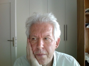 Andrzej Coryell w białej koszuli, z siwymi włosami, opiera głowę na dłoni