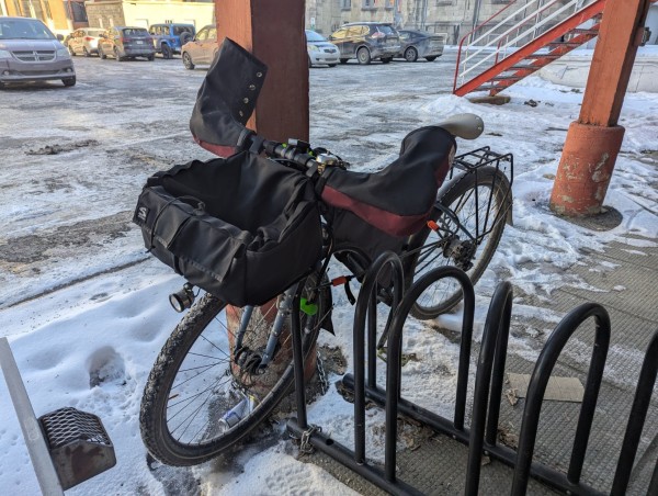 Bike on a rack with snow. The bicycle has special equipment for winter cycling, such as lights and fabric to protect the hands from cold and wind.