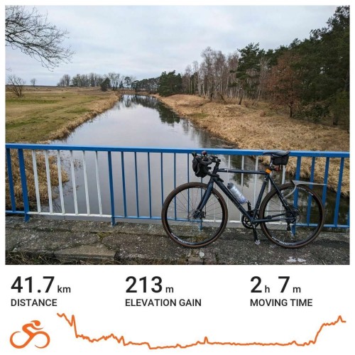 Karta aktywności z serwisu Ride with GPS. Na zdjęciu rower oparty o biało-niebieską barierkę mostu nad rzeką widoczną w tle. Poniżej statystyki: dystans 41,7 km, przewyższenia 213 m, czas w ruchu 2g 7m.