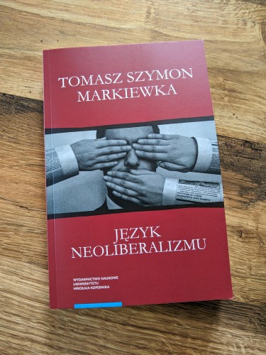 Książka „Język neoliberalizmu” Tomasza Szymona Markiewki leży na drewnianym stole. W centrum jest zdjęcie osoby z oczami i ustami zasłoniętymi dłońmi wystającymi z rękawów z gazet. Nad zdjęciem na ciemnoczerwonym tle imiona i nazwisko autora, pod tutuł. W lewym dolnym rogu nazwa wydawnictwa: Wydawnictwo Naukowe Uniwersytetu Mikołaja Kopernika.