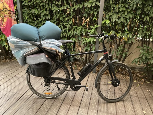 Rower z załadowanym bagażnikiem po zakupach w meblowym: dwie giga-poduchy, kilka chodników, wypełniona sakwa. 