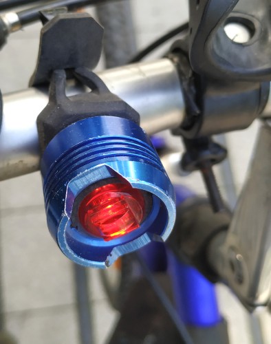Malutka granatowa tylna lampka rowerowa zamontowana tymczasowo na kierownicy.