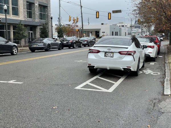 A buffered bike lane obstructed by cars parked in the curb-side bike lane rather than in the marked parking spaces intended as a buffer between the bike lane and traffic lane