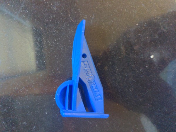 A blue plastic triangular tool with a small semi circle at one end.  It is embossed with the brand name "tyre glider".