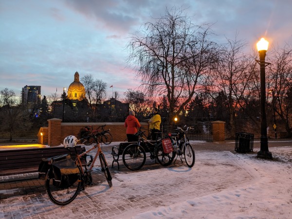 Sunrise photo of winter cyclists commuting in January. Snowy ground and pink sunrise. 