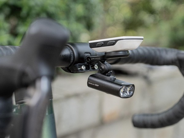 Bicycle handlebars showing a bracket fixed to the handlebar clamp that has a Garmin unit attached on top and a light underneath 
