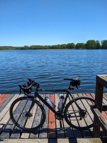 Rower szutrowy stoi na drewnianym pomoście, za nim widoczne jezioro.