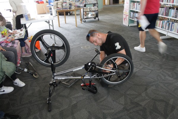 Ben sitting on the floor of Barry library beside an upside down bike which he is working on.