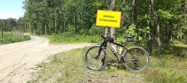 Rower oparty o tabliczkę "Droga czołgowa", obok leśna szutrowa droga