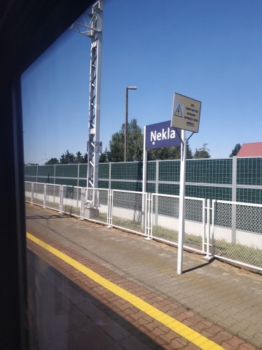 Zdjęcie z pociągu, za szybą jest tablica stacji Nekla